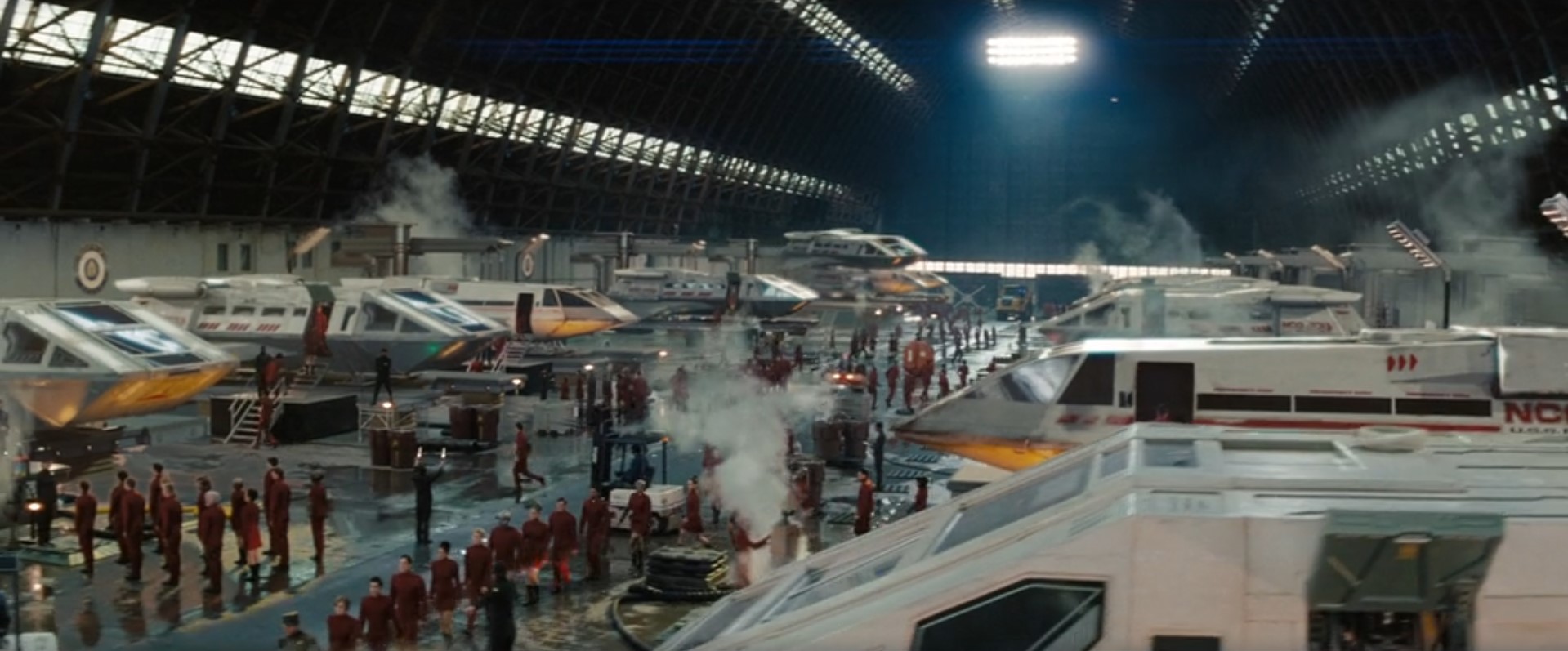 A hangar with an arched roof supported by girders, a concrete floor, and shuttlecraft lining the long walls.